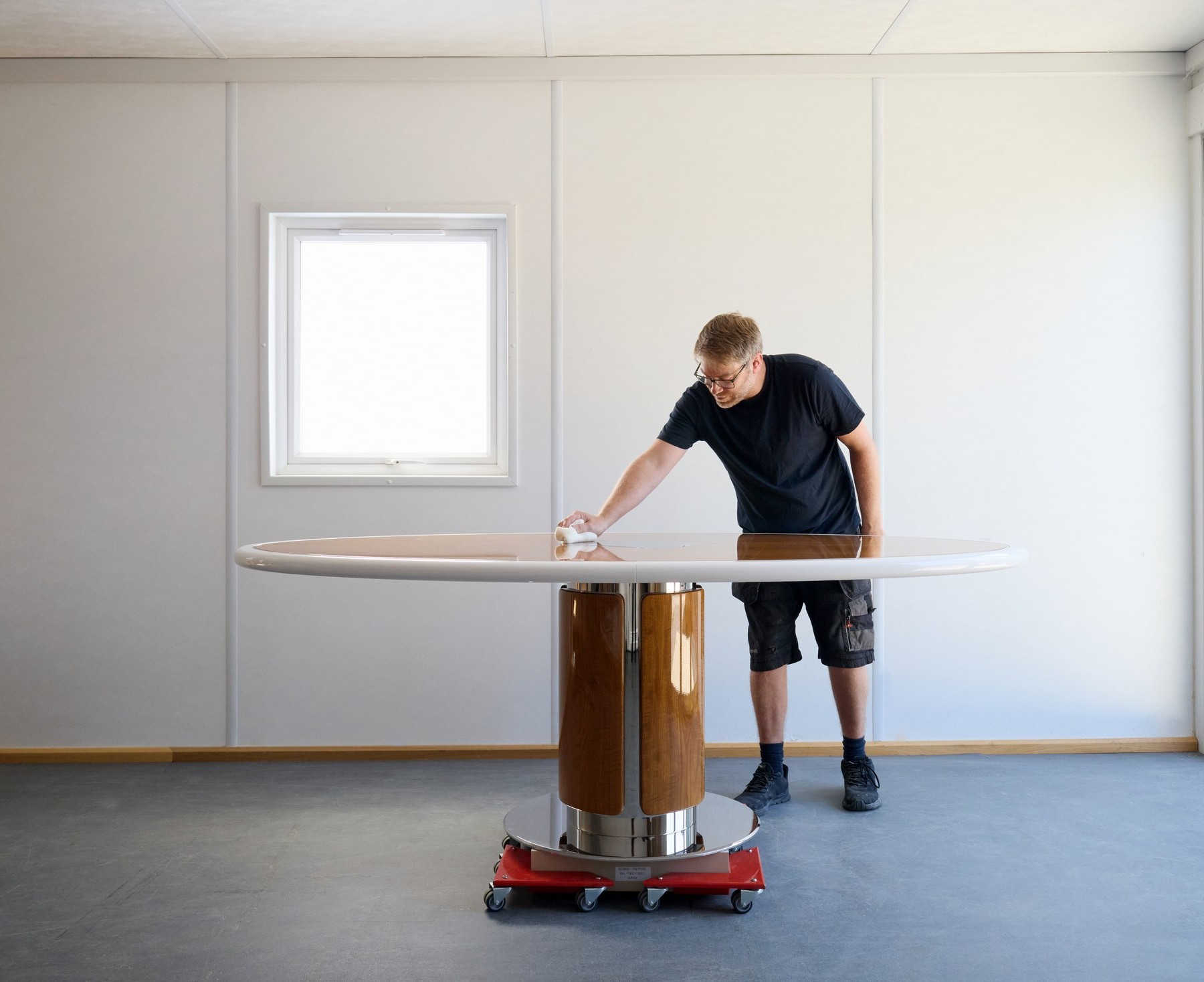 Hand-polishing the surface of a round table with a chrome and walnut pedestal
