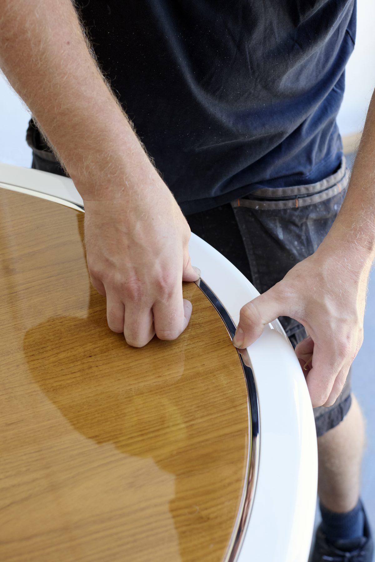 Fitting a stainless-steel edge trim to a CNC-shaped teak table for a yacht interior